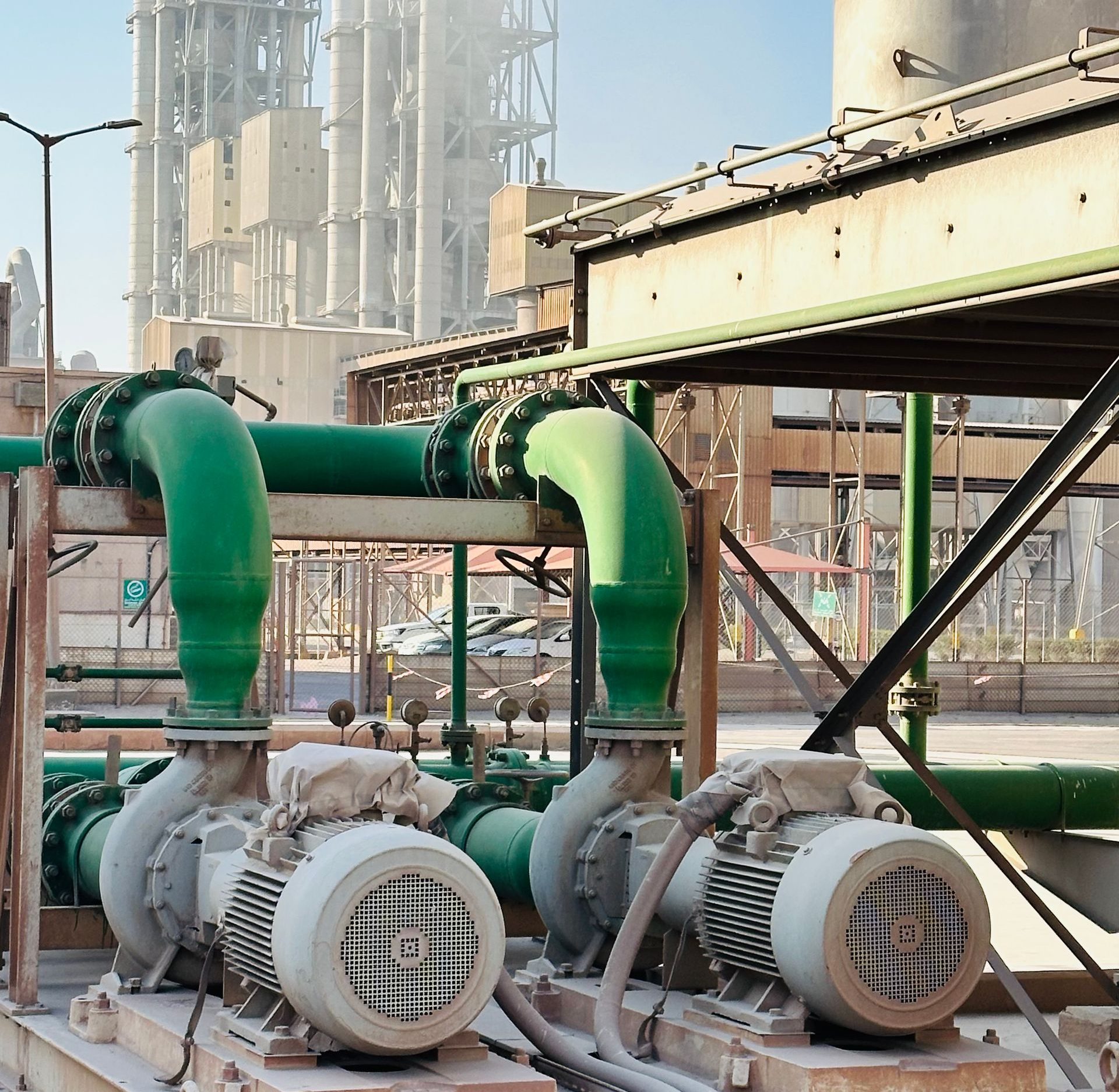 Outdoor scene of industrial machinery with distinct green pipes at a large factory.